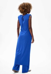 Długa niebieska sukienka o gładkiej fakturze, z rękawami typu cap oraz szczegółem w postaci wiązania z tyłu. Posiada rozcięcie u dołu i szerokie nogawki.