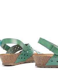 Sandalias de cuero verde con diseños perforados, tacones de cuña de corcho y correas traseras ajustables, exhibiendo un acabado texturizado y cortes únicos.