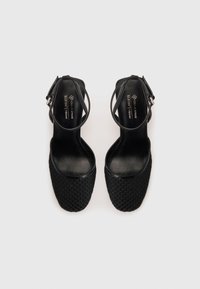 Scarpe con tacco alto nere caratterizzate da una tomaia in rete testurizzata, dettagli in pelle lucida, cinturini alla caviglia regolabili e una punta quadrata.