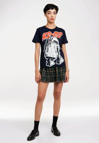 Navy T-shirt featuring a graphic of R2-D2, paired with a green plaid pleated skirt. Black shoes and socks complete the outfit.