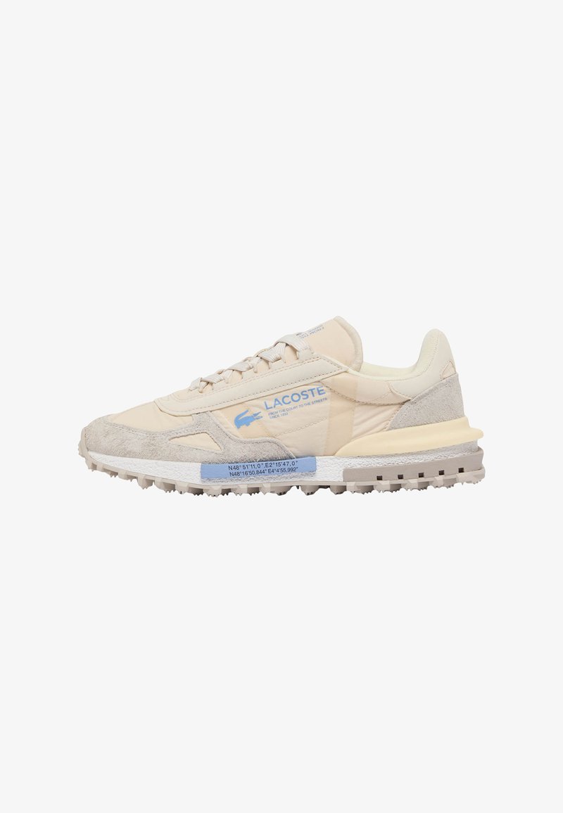 Zapatilla beige de Lacoste con detalles en ante, texto del logo en azul y coordenadas geográficas azules en la suela intermedia blanca, sobre fondo blanco.