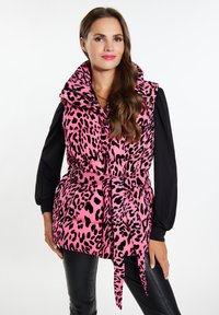 Weste mit pinkem Leopardenmuster, hochgeschlossen, mit tailliertem Schnitt und Seitentaschen, getragen über einem schwarzen Langarmshirt. Glatte Textur und puffiges Design.