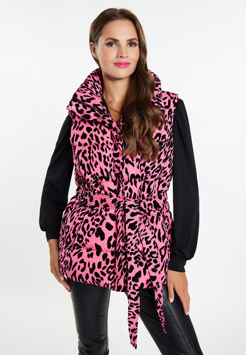 Weste mit pinkem Leopardenmuster, hochgeschlossen, mit tailliertem Schnitt und Seitentaschen, getragen über einem schwarzen Langarmshirt. Glatte Textur und puffiges Design.