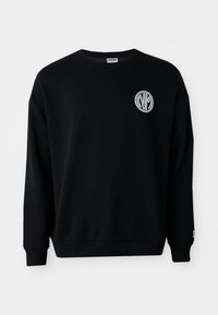 Svart hettegenser laget av mykt stoff, med rund hals, lange ermer og en liten brodert logo på brystet.
