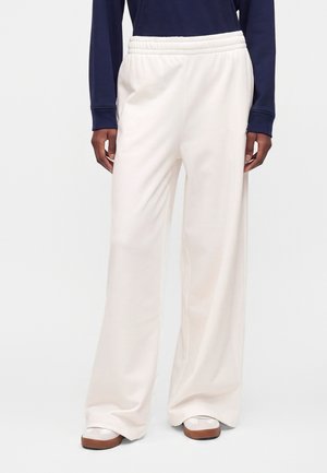 Person iført løstsiddende hvide bukser med elastisk talje, navy bluse med lange ærmer og hvide sneakers med brune såler.