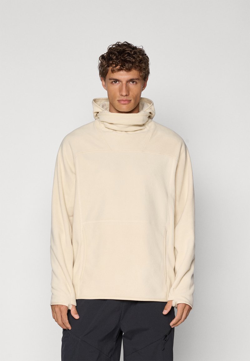Beige fleece pullover with a high collar, front pocket, and long sleeves. Soft texture with stitching details. Dark pants not shown.