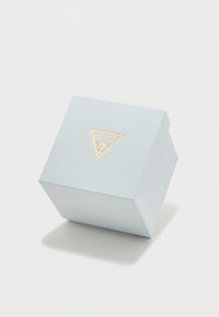 Φωτεινό μπλε υφασμάτινο ορθογώνιο κουτί με χρυσό τριγωνικό λογότυπο στην μπροστινή πλευρά. Το κουτί έχει λεία επιφάνεια και ελαφρώς κεκλιμένη κορυφή.