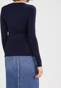 Navy long-sleeve top made of smooth fabric paired with a blue denim skirt featuring a central seam and two back pockets.