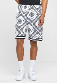Zwart-witte korte broek met een bandana-patroon, een elastische tailleband en een witte rand aan de zoom, gecombineerd met witte sneakers en sokken.