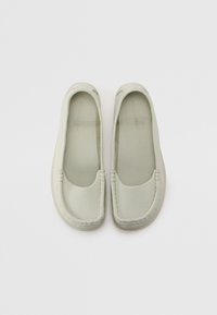 Mocassins en cuir gris clair avec une texture lisse, un bout arrondi et des accents cousus le long du bord supérieur. Semelles en caoutchouc plates.