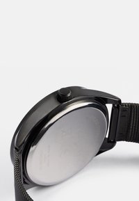 Sort rustfrit stål ur med et glat rundt urkasse, et struktureret mesh-rem og en lille krone på siden til justering af tiden.