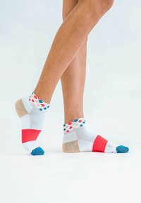 Bunte gemusterte Knöchelsocken in Weiß, mit roten, blauen und beigen Akzenten, einem Rautenmuster am Bündchen und einer verstärkten Zehenpartie.