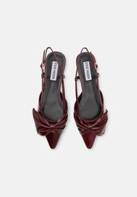 Tacchi slingback in pelle verniciata bordeaux con punte appuntite, dettaglio anteriore annodato e cinturini sottili. Presentano una morbida fodera interna nera.