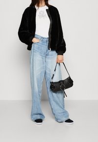 Sort faux fur bomberjakke, hvid grafisk t-shirt, lyseblå brede jeans og sort crossover-taske. Tilbehøret inkluderer en kædedetalje.