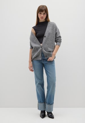 Gray knit cardigan with two buttons, front pockets, worn over a black top. Blue wide-leg jeans with folded cuffs and black pointed-toe boots.