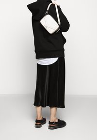 Czarna bluza z kapturem, biała koszula pod spodem, czarna satynowa spódnica midi oraz czarne sandały. Kremowa torebka na ramię z geometrycznym wzorem.