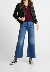 Sort læder bikerjakke over en bordeaux top, parret med høj talje, brede blå denim jeans og sorte høj-tops sneakers.