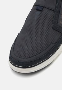 Marineblå slip-on sko med struktureret mesh-overdel, kontraststing og en hvid gummisål med en strømlinet form.
