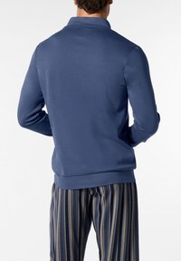 Felpa blu marina con collo, texture liscia e orlo a coste, abbinata a pantaloni larghi a righe blu e crema.