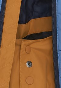 Blå quiltad yttertyg med en mörk marinblå foder. Har orange inre tyg, tryckknappsstängning och detaljerade sömnadsmönster.