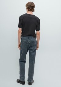 Sort t-shirt med korte ærmer sat sammen med blegede grå jeans. Jeansene har lige skæring og baglommer. Modellen har sorte sko på.