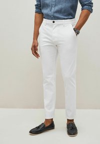 Pantaloni bianchi su misura con una vestibilità slim, realizzati in cotone. Presentano una chiusura con bottone e tasche. Abbinati a mocassini neri.