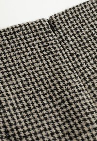 Wollen stof met een houndstooth-patroon in zwart en crème. Heeft een zichtbare rits bij de naad, wat een textuur geeft aan het oppervlak.