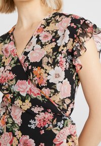 Robe portefeuille florale en tissu noir avec des manches volantes. Présente des fleurs roses et blanches avec des feuilles vertes et une bordure orange le long de l'encolure.