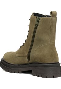 Bota de ante verde olivo hasta el tobillo con una suela marrón gruesa, parte delantera con cordones y una cremallera lateral para un fácil acceso. Acabado texturizado y diseño robusto.