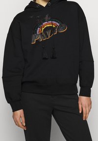 Hoodie noir avec un design coloré et brodé en arc-en-ciel et le texte "PUMA", ornée de pampilles sur les cordons de serrage et d'une coupe décontractée.