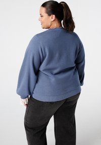 Blauwe gebreide trui met een relaxte pasvorm, verlengde schouders en geribde manchetten. Gecombineerd met zwarte wijde jeans. Textuurstof.