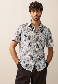 Camicia a maniche corte in tessuto leggero con stampa floreale tropicale dai toni blu, verdi e marroni; colletto con bottoni.
