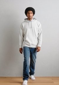 Sweatshirt cu glugă de culoare gri deschis, prevăzut cu buzunar tip cangur, asortat cu blugi denim de culoare albastră. Tenisi albi completează ținuta.