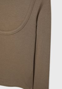 Zbliżenie na brązową, prążkowaną koszulę z długim rękawem, ukazującą dekolt i szew boczny na jasnym tle.