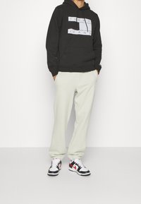 Černá mikina s kapucí a logem "TOMMY JEANS", krémové tepláky a černé/bílé/červené tenisky. Neformální, volný střih a měkké materiály.