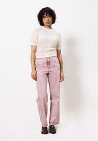 Hellbeige, kuscheliger Strickpullover mit kurzen Ärmeln, kombiniert mit hellrosa, hochgeschnittenen, gerade geschnittenen Jeans und braunen Slippern.