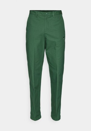 Pantalones verdes confeccionados en una tela suave, con un corte estándar, frente plano y un pequeño logotipo en la parte cerca de la cintura.