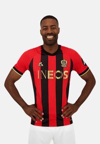 Maillot de football rayé rouge et noir avec col rond, logo INEOS doré sur le devant, manches courtes et bordures dorées.