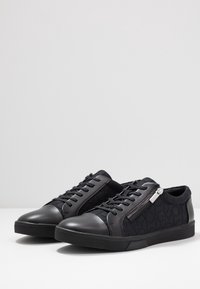 Černé tenisky vyrobené z hladké kůže a strukturované tkaniny s logovým vzorem, kulatá špička, šněrování a zipový detail.