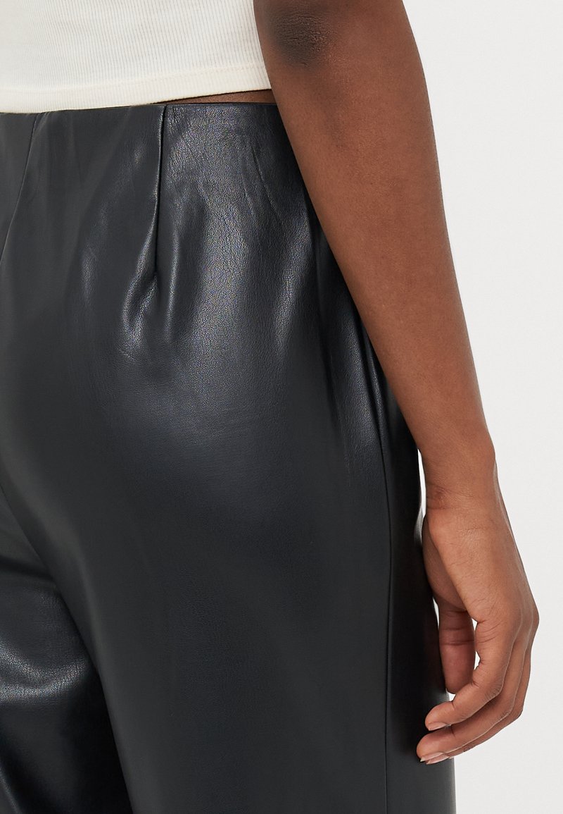 Černé kožené kalhoty s hladkým povrchem, s předními sklady, vysokým pasem a uvolněným střihem, zobrazené spolu s bílým žebrovaným topem.