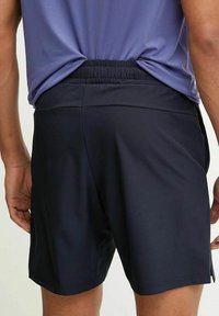 Pantaloni da atletica navy con elastico in vita, caratterizzati da una texture liscia e una lunghezza corta. La vista posteriore mostra l'assenza di tasche e dettagli minimi.