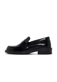 Mocasines de cuero negro con un acabado suave, punta redondeada, tacón bajo en bloque y una correa decorativa en la parte superior. Detalles texturizados en los laterales.