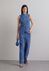 Blue woven vest and pants set, featuring a fitted design, buttons, and two front pockets. Accessorized with a blue handbag and patterned shoes.