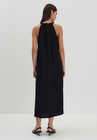 Abito nero con collo halter dotato di una cintura legata sulla schiena, silhouette fluente e tessuto leggero, che arriva alla caviglia con una texture morbida.