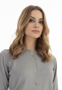 Grauer, langärmliger Cardigan aus Strickstoff mit rundem Ausschnitt und sieben hellbraunen Knöpfen auf der Vorderseite. Weicher Stoff, leichtes Design.