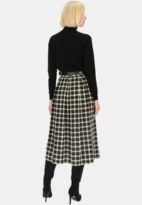 Czarny sweter z golfem w połączeniu z spódnicą w kratę w kolorze czarno-białym o długości do kolan, z wcięciem w talii i czarnym paskiem.