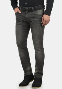 Pantalones de mezclilla gris con un corte ajustado, que presentan un ligero desgaste, cinco bolsillos y un cinturón negro. Combinados con botas negras por el tobillo.