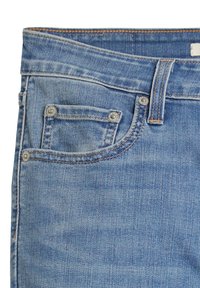 Jeans de denim azul claro con un acabado texturizado, que presentan un pequeño bolsillo frontal, remaches de metal y costuras en contraste a lo largo de los bordes.