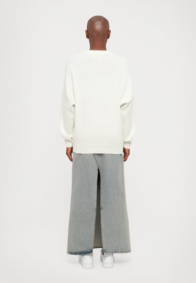 White knit sweater with oversized sleeves paired with a light blue denim maxi skirt featuring a high slit, worn with white sneakers.