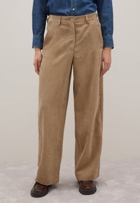 Beige Cord-Ripp-Hose mit weitem Bein und vertikaler Rippstruktur, mit einem Frontknopfverschluss und Seitentaschen, getragen mit einem Jeanshemd.